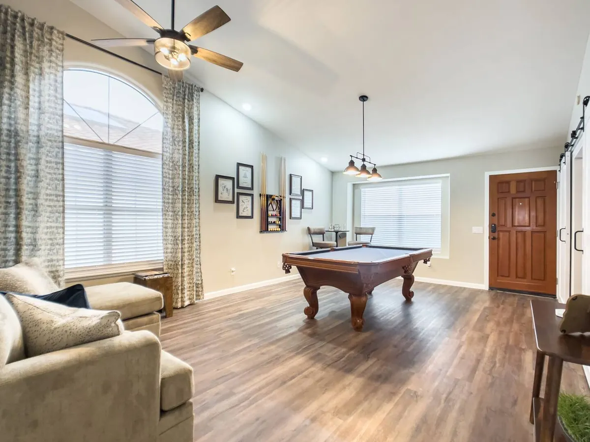 A spacious and inviting interior with a pool table, comfortable sofa, welcoming front door, artistic wall art, and soft lighting. The layout encourages gatherings, gaming, and relaxation, embodying a casual yet energetic entertainment space.
