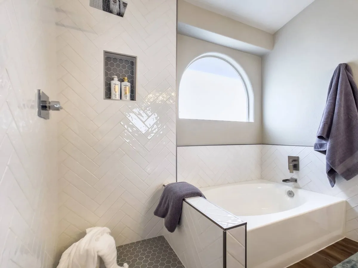 A spa-like bathroom featuring a freestanding bathtub, a newly retiled shower niche with hexagonal tiles, and an arched window that lets in natural light. The atmosphere is peaceful and rejuvenating, perfect for relaxation and self-care.