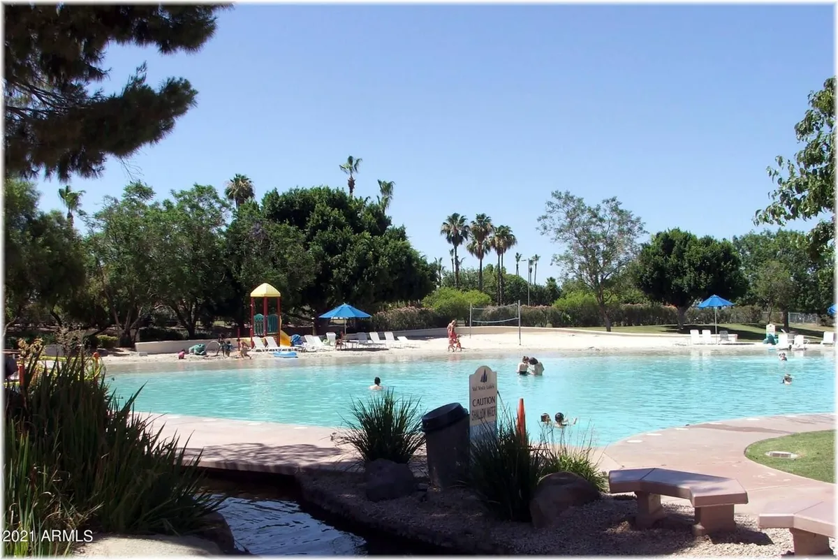 This image captures a vibrant outdoor scene with a sparkling swimming pool, a nearby playground structure for children, palm trees, and inviting lounge chairs around the pool. The atmosphere is bright and joyful, suggesting fun under the sun and family gatherings in a lively setting.