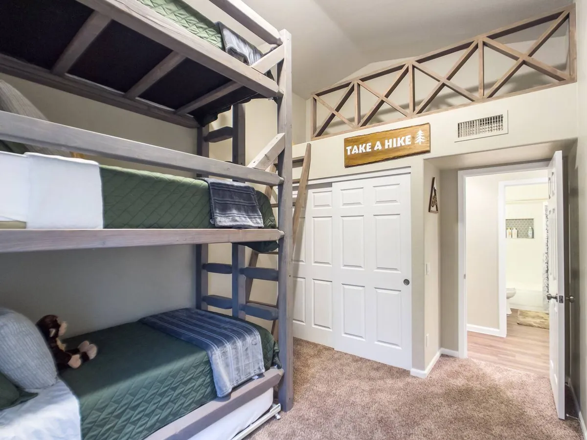 A playful bedroom with bunk beds, a 'Take a Hike' sign on the wall, and plush toys on the beds. The design is fun and inviting, suitable for children or guests seeking a cozy nook to rest and play.