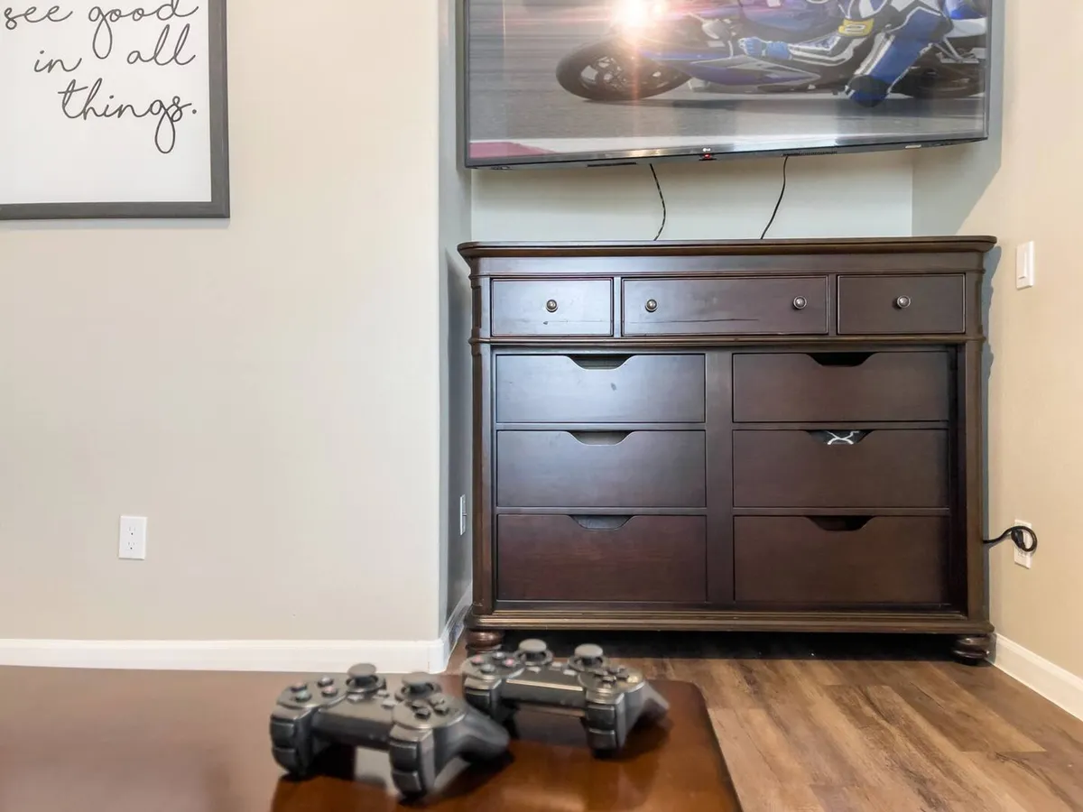 A cozy gaming den with a visible gaming console, wooden dresser, and wall art. The set-up is casual and inviting, emphasizing dedicated gaming or movie sessions in a relaxed environment.