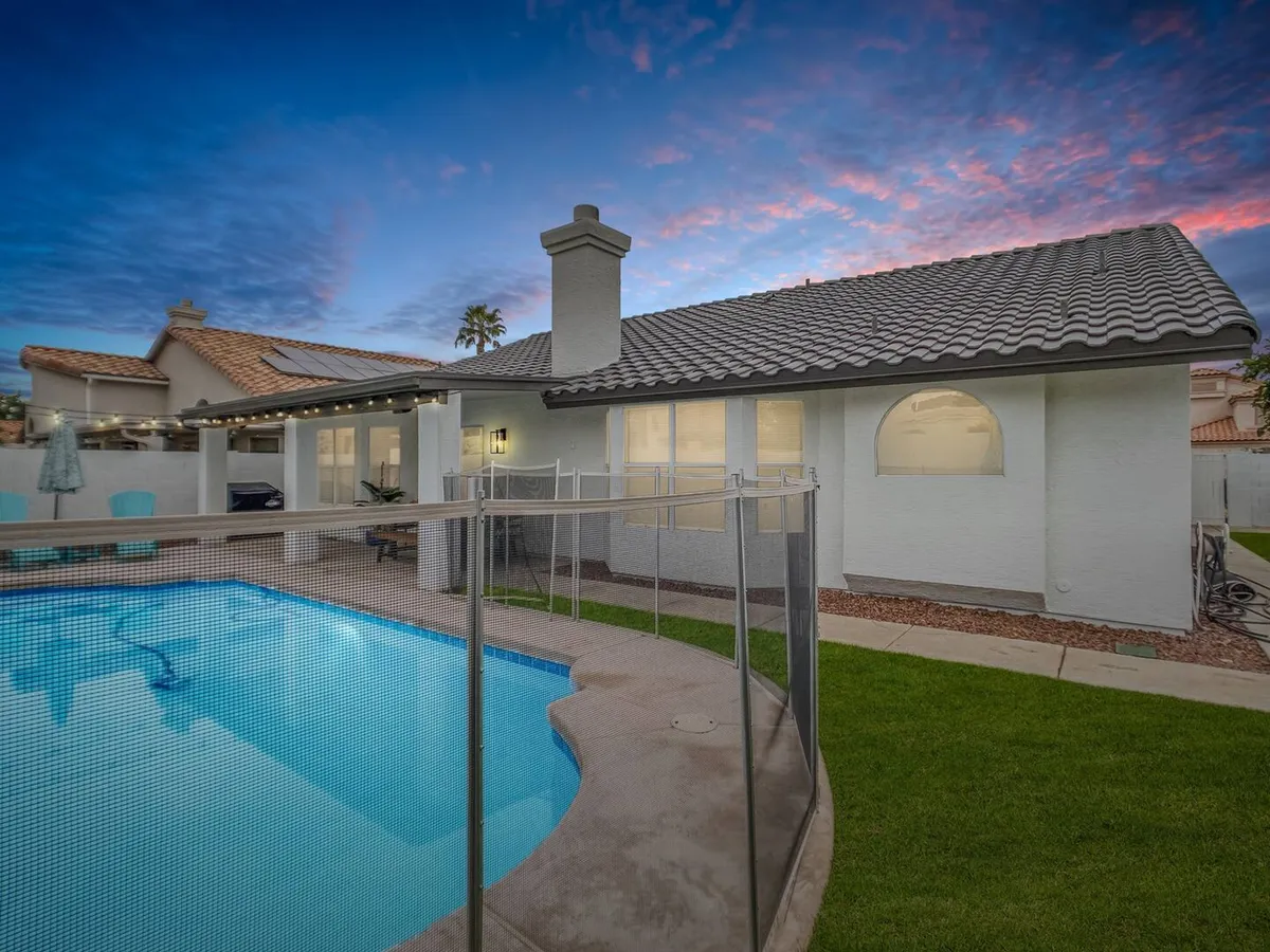 This image showcases a tranquil backyard with a swimming pool, surrounded by a spacious patio and lush landscaping. The house exterior is visible, providing a sense of the home's scale and inviting atmosphere. The scene suggests opportunities for both relaxation and informal team gatherings outdoors, with comfortable seating and a setting ideal for post-work chats or evening swims.