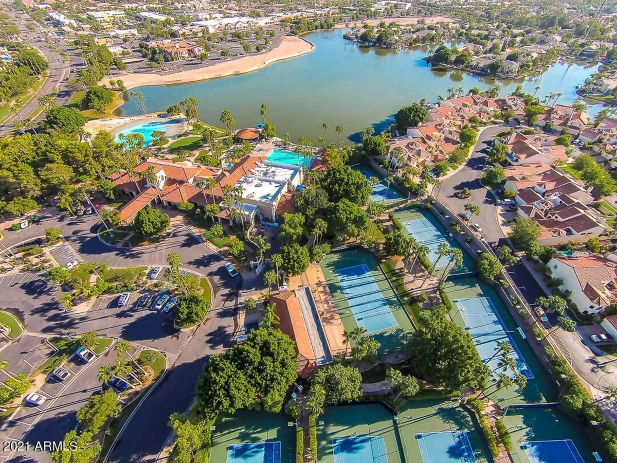 An expansive view of a community area featuring multiple swimming pools, tennis courts, a scenic lake, lush greenery, and surrounding residential buildings. The landscape invites exploration and highlights the variety of recreational options available for families.