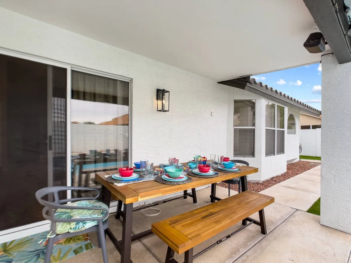 A cheerful outdoor dining table set with colorful dishware sits in a welcoming patio area. The setup is ideal for hosting outdoor meals, brunches, or celebratory dinners with friends and family. Casual seating arrangements encourage conversation and togetherness.