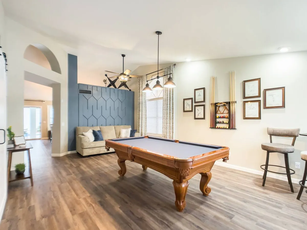 A vibrant great room featuring a sleek pool table set as the focal point. The room is accented by a plush sofa, stylish wall decorations, and modern light fixtures, creating a fun and welcoming atmosphere ideal for socializing and friendly competition.