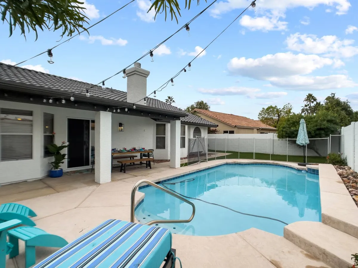 A sparkling swimming pool is surrounded by comfortable outdoor seating and lush landscaping. String lights are draped above the seating area, creating a festive and inviting ambiance ideal for social gatherings or group relaxation. The space feels open and cheerful, perfect for poolside fun or evening get-togethers.