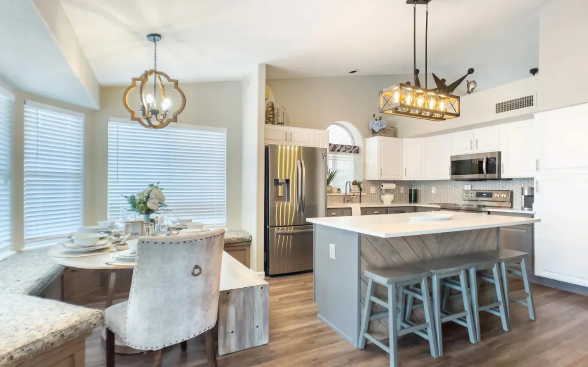 A warm, inviting kitchen and dining area with a prominent kitchen island, dining nook, chandelier, and gleaming stainless steel appliances. The setting radiates a sense of comfort and celebration, perfect for family meals or hosting guests. Ample counter space and thoughtful built-ins are visible, supporting a seamless cooking and dining experience.